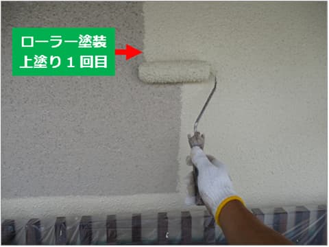 戸建て住宅の外壁にローラーで中塗り塗料を塗装している状況
