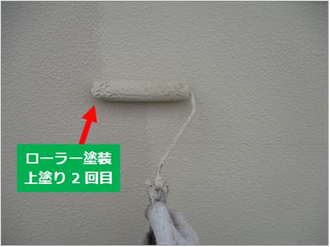 戸建て住宅の外壁にローラーで上塗り塗料を塗装している状況