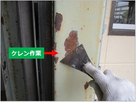 倉庫入り口シャッター枠鉄骨の、剥離した劣化塗膜を金ベラで除去している状況。