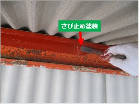 倉庫のひさしの鉄骨に刷毛で錆止め塗装を施工している状況