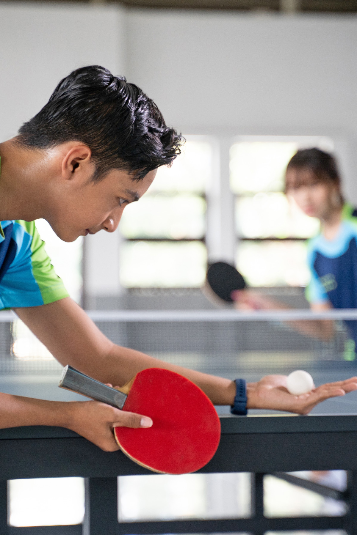 Ein Tischtennisspieler in sportlicher Kleidung bei einem Aufschlag, der Ball ist als Bewegungsunschärfe in seiner Hand zu sehen.